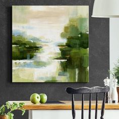 an abstract painting hangs on the wall above a dining room table with two green apples