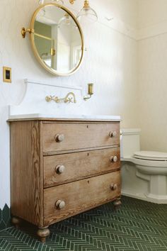 a white toilet sitting next to a wooden dresser in a bathroom under a round mirror