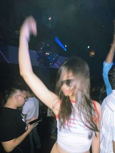 a woman dancing at a party with her arms in the air and other people standing around