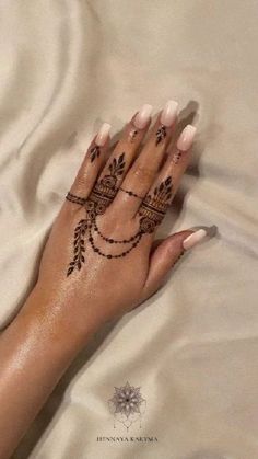 a woman's hand with henna tattoos on her left wrist and fingers, resting on a bed sheet