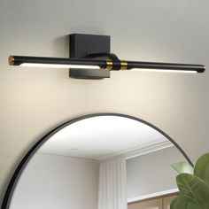 a black and gold bathroom light fixture on a white wall with a mirror in the corner