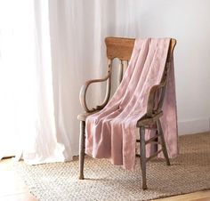 a chair with a pink blanket draped over it in front of a white wall and window