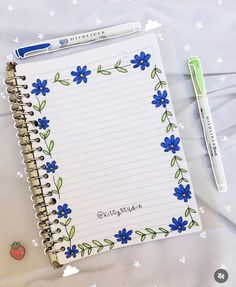 an open notebook with blue flowers and green leaves on it, next to a pen