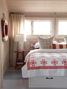 a bed with red and white pillows in a bedroom next to a window on the wall