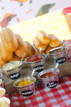 hot dogs and other condiments are displayed on a table with red checkered cloth