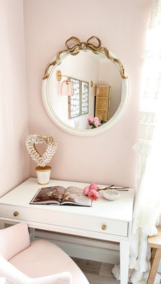 a white desk topped with a mirror next to a pink chair and flower vase on top of it