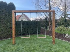 a wooden swing set with two swings in the grass