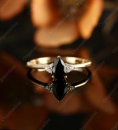 a black diamond ring sitting on top of a table next to an orange flower with petals in the background