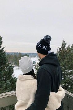 a man and woman standing on top of a wooden deck with trees in the background