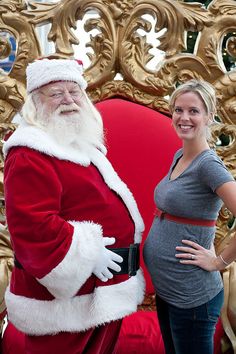 a pregnant woman standing next to santa clause