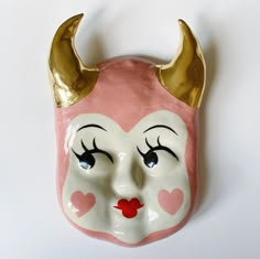 a ceramic mask with horns and hearts painted on it's face is shown against a white background