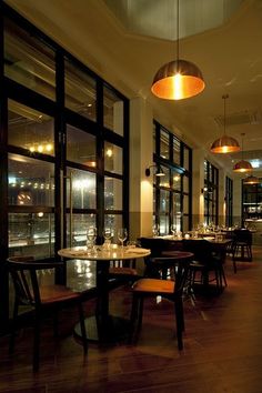 an empty restaurant with tables and chairs in front of large windows overlooking the city at night