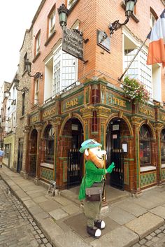 an inflatable green man stands outside the entrance to a brick building on a cobblestone street