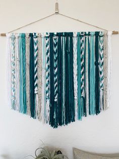 the wall hanging is decorated with different colored yarns and tassels, along with a potted plant