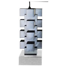 a tall metal sculpture sitting on top of a cement block next to a white wall