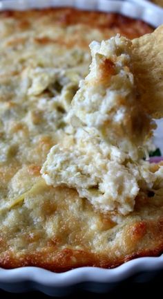 a hand dipping a cracker into a casserole dish