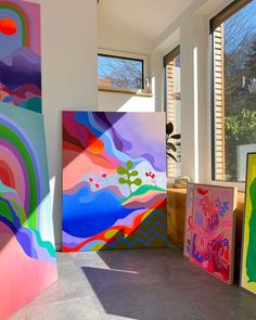 three colorful paintings are on display in front of large windows