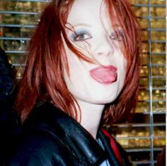 a woman with red hair and blue eyes making a funny face while wearing a leather jacket