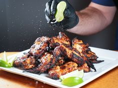 a person in black gloves is sprinkling sauce on chicken wings with limes