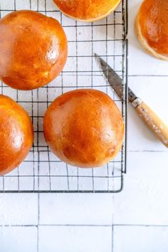 four orange buns sitting on a cooling rack with a knife next to them,