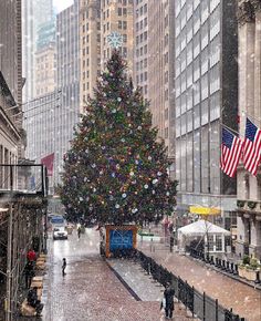 a large christmas tree in the middle of a city street with snow falling on it