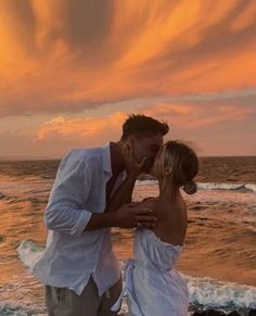 a man and woman kissing on the beach with sunset in the backgroung