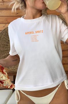 Introduce our trendy and comfortable Aperol Spritz T-Shirt! Show off your love for this delicious cocktail with this stylish shirt. Featuring a bold "Aperol Spritz" print on the front with a list of its classic ingredients. This crewneck is perfect for any casual occasion. Made from high-quality, soft and comfortable material, it's perfect for any weather. It's also a great gift for any loved one who is a fan of Aperol Spritz. Order yours today and raise a glass to good times in style! Perfect a White Graphic Print T-shirt For Brunch, Casual Screen Print T-shirt For Brunch, White Crew Neck T-shirt For Brunch, Summer Brunch T-shirt With Screen Print, Screen Print Crew Neck T-shirt For Brunch, Crew Neck T-shirt With Screen Print For Brunch, Trendy Summer T-shirt For Brunch, Graphic Tee With Screen Print For Brunch, Casual Screen Print Top For Brunch