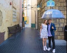 two people are standing under an umbrella on the street in front of a stone building