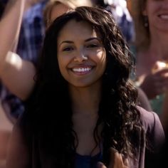 a woman with long dark hair smiling and holding her hands up in the air while others look on