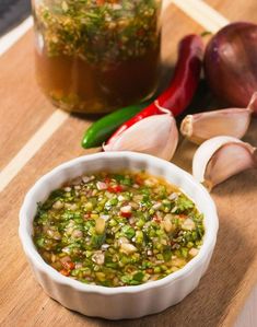 a white bowl filled with green sauce next to garlic and red peppers on a cutting board