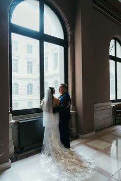 a bride and groom standing in front of a large window