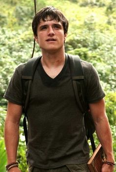 the young man is carrying two books in his hands while walking through the woods with trees and bushes behind him