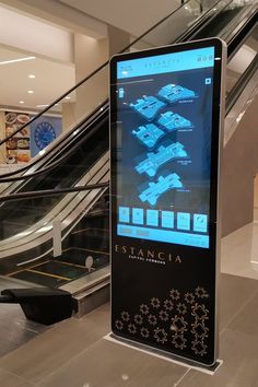 an escalator with a large screen on it in the middle of a building