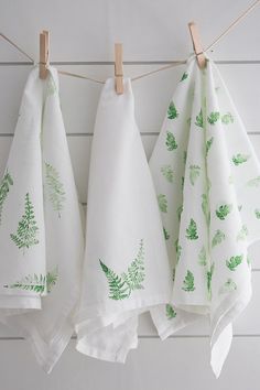 three tea towels hanging on clothes pins with green leaves and ferns printed on the front