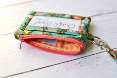 a small wallet with a name tag attached to it on a white wooden table next to a keychain