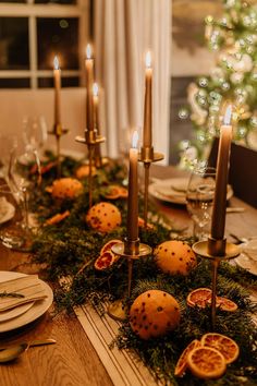 the table is set with oranges, candles and greenery for a festive look