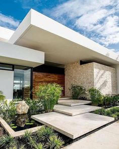 a modern house with plants and rocks in the front yard