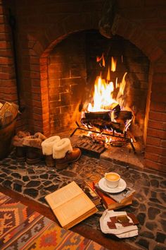 an open book on the floor in front of a fireplace with a cup of coffee next to it