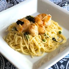 pasta with shrimp and spinach in a white bowl on a blue patterned tablecloth