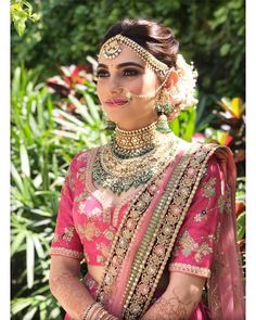 a woman wearing a pink and gold bridal outfit with jewelry on her neck, standing in