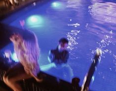 two people are sitting in the middle of an indoor swimming pool at night with lights on