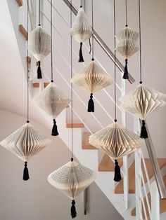 several white paper lanterns hanging from the ceiling in front of some banisters with black tassels