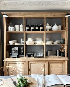 an open book sitting on top of a table next to a wooden shelf filled with dishes