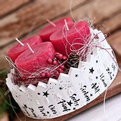 some red candles are in a white bowl on a wooden tray with christmas decorations around it