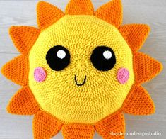 a crocheted sunflower with big eyes on a white wooden background, it looks like the face of an animal