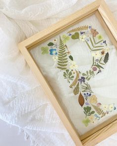 a wooden frame with embroidered flowers and leaves on it sitting on a white cloth covered surface