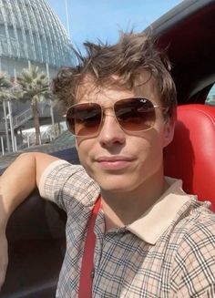 a man wearing sunglasses sitting in the back seat of a car with palm trees behind him