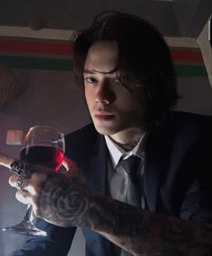 a man in a suit holding a glass of red wine and pointing to the side