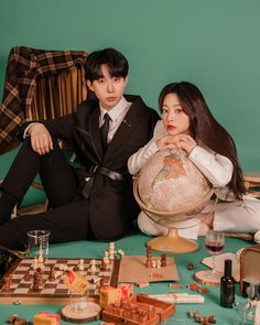 a man and woman sitting on the floor next to a globe with chess pieces all over it