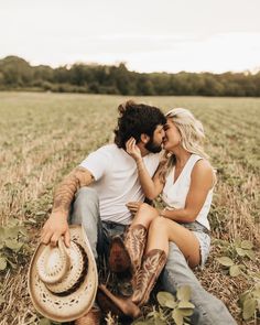 a man and woman sitting on the ground in a field with cowboy hats around their necks